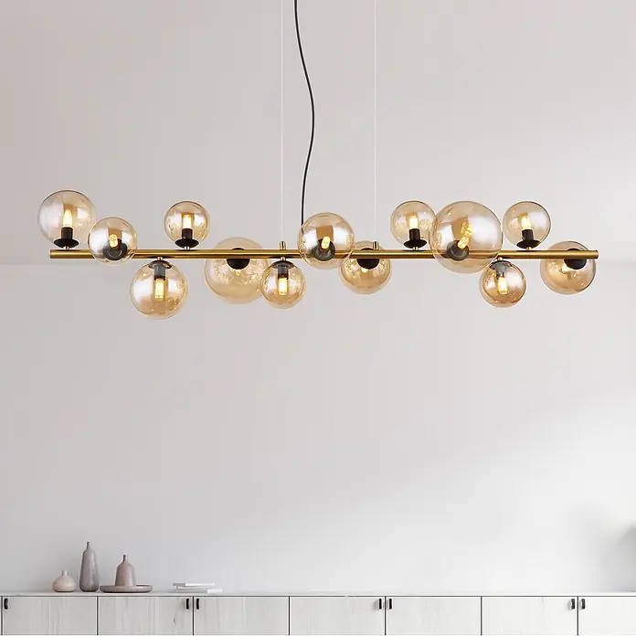 Globo Pendelleuchte Riha - L x B x H: 1.200 x 345 x 1.200 mm, G9 - Lineare Pendelleuchte mit goldener Stange und mehreren bernsteinfarbenen Glaskugelschirmen über einem hellen Holzschrank.