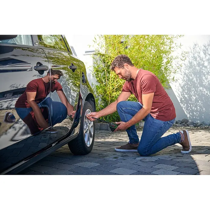 Bosch Akku-Luftpumpe Pneo - 3,6 V, Max. Druck: 10,3 bar - Mann nutzt grünen und schwarzen Bosch Akku-Kompressor, um den Druck eines schwarzen Autoreifens zu prüfen und einzustellen.