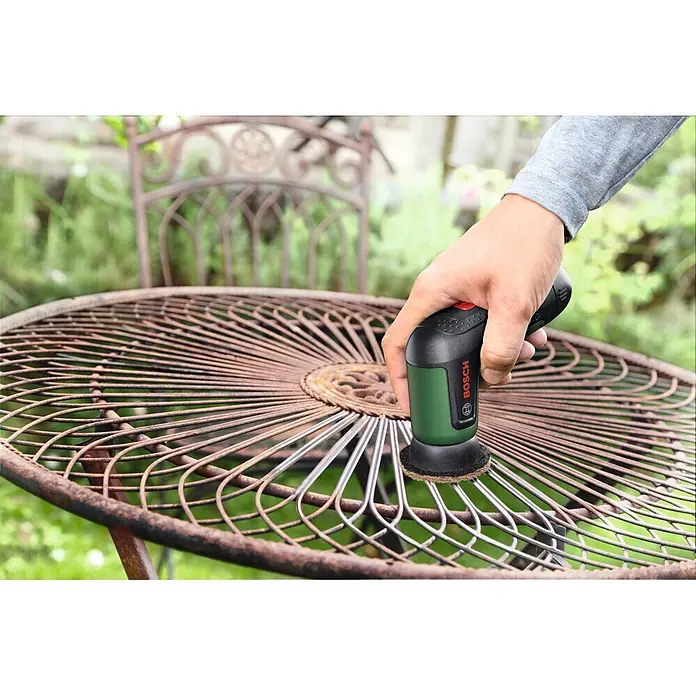 Bosch Akku-Reinigungsbürste Taydo - 3,6 V, 1 Akku, 6 -tlg. - Hand benutzt grünen Bosch Mini-Schleifer, um Rost von einem Metall-Gartentisch zu entfernen.