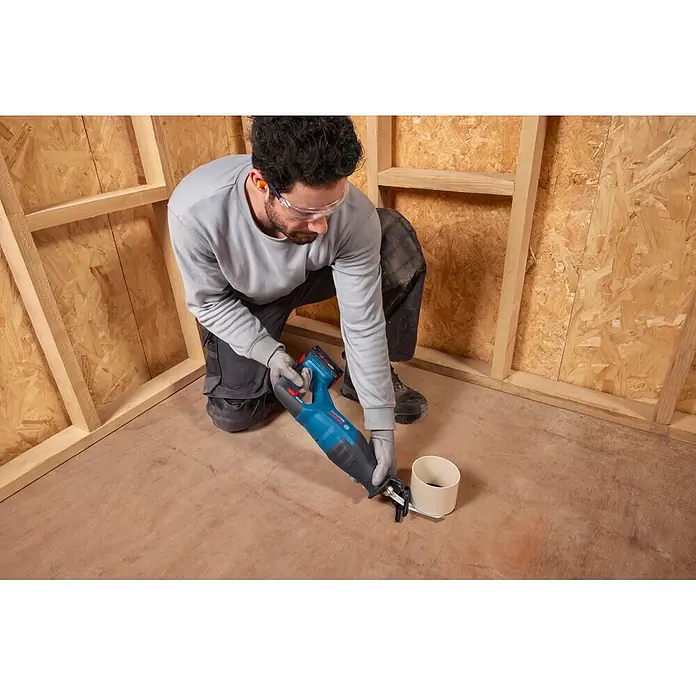Bosch Professional AMPShare 18V Akku-Säbelsäge GSA18V-280 - 18 V, Ohne Akku, Leerlaufhubzahl: 0 /min - 3.100 /min, Inkl. L-Boxx - Eine Person sägt mit einer blauen Säbelsäge ein weißes Rohr auf einem Holzfußboden.