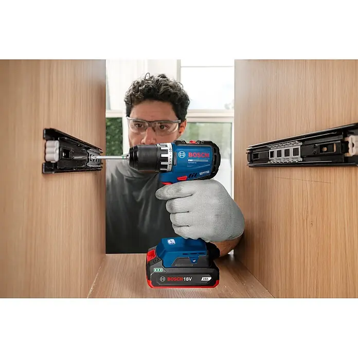 Bosch Professional AMPShare 18V Akku-Bohrschrauber GSR18V-52 - 18 V, Ohne Akku, 70 Nm, Ohne Akku - Eine Person benutzt einen blau-schwarzen Bosch Akku-Bohrschrauber mit 18V-Akku, um einen Schubladenauszug in einem Holzschrank zu montieren.
