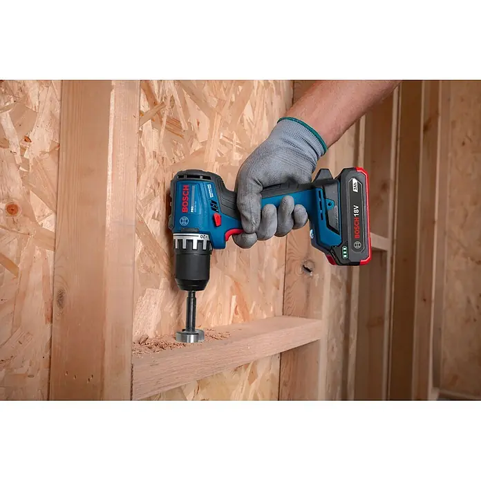 Bosch Professional AMPShare 18V Akku-Bohrschrauber GSR18V-52 - 18 V, Ohne Akku, 70 Nm, Ohne Akku - Eine behandschuhte Hand bohrt mit einem blau-schwarzen Bosch Akkubohrschrauber und rotem 18V Akku ein Loch in einen Holzbalken.