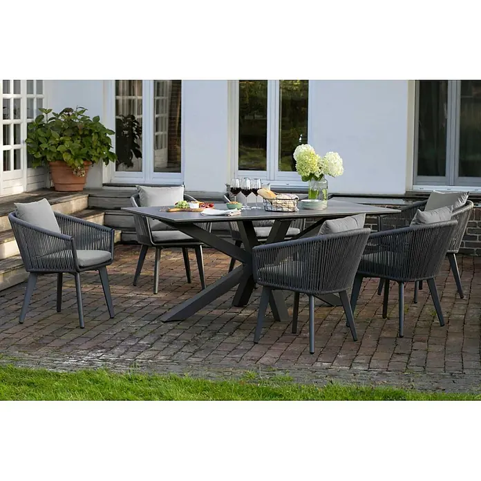 Bene Living Gartentisch Almeria - L x B x H: 200 x 90 x 76 cm, Aluminium Gestell mit gesinnerter Tischplatte aus Keramik, Rechteckig, Hellgrau - Graue Outdoor-Essgruppe: rechteckiger Tisch, sechs geflochtene Stühle mit Kissen, auf einer Terrasse mit Speisen und Getränken.