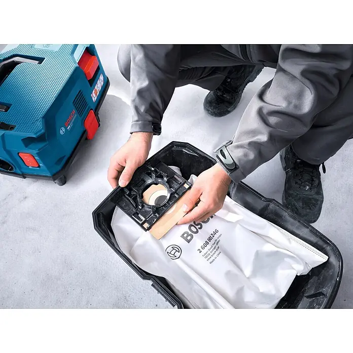 Bosch Professional Elektro-Nass- & Trockensauger GAS12-25LS - 1.200 W, Behältervolumen: 25 l, Halbautomatisch - Hand setzt einen weißen Bosch Staubsack in einen blauen Bosch Sauger ein.