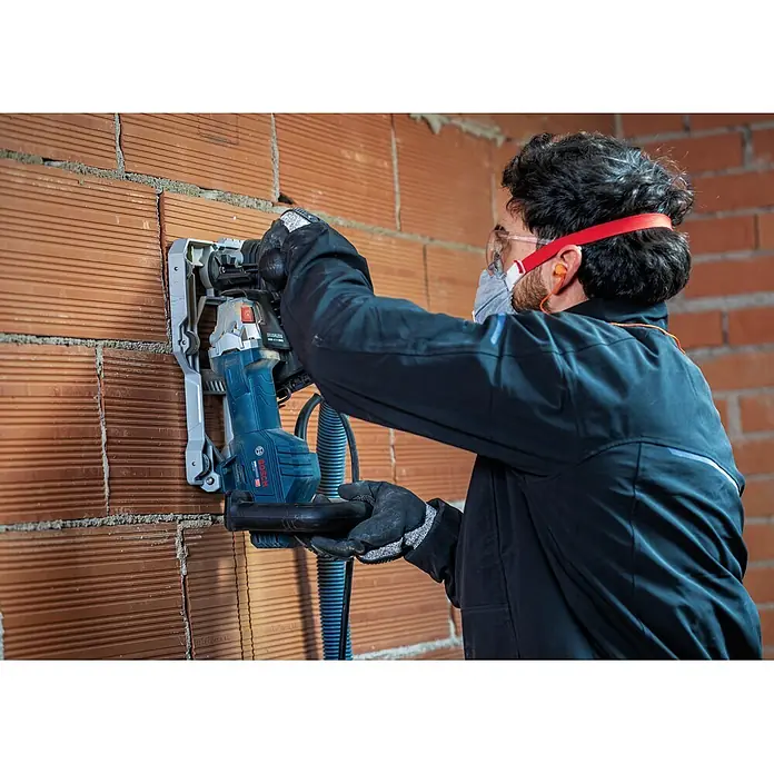 Bosch Professional Mauernutfräse GNF20-40 - 2.000 W, Durchmesser Scheibe: 150 mm - Eine Person in Schutzkleidung benutzt eine blau-graue Bosch Mauernutfräse, um eine Nut in eine rote Ziegelwand zu schneiden.