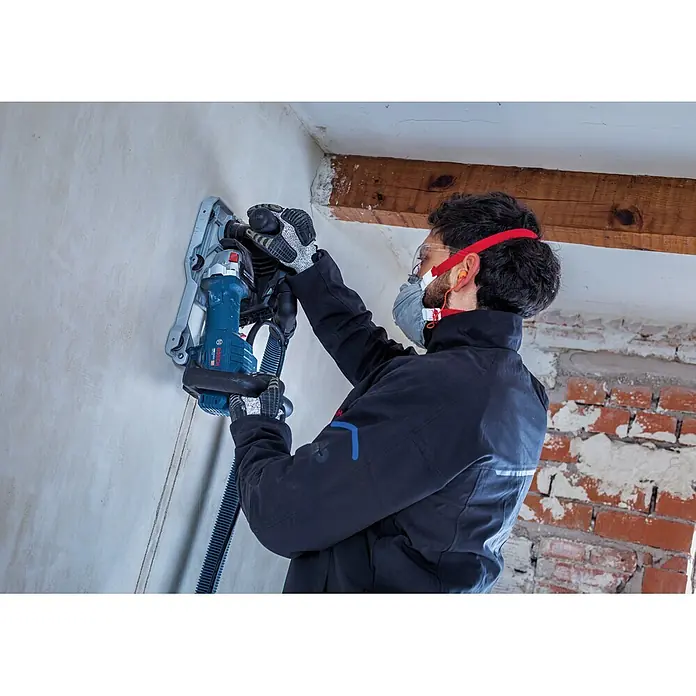 Bosch Professional Mauernutfräse GNF20-40 - 2.000 W, Durchmesser Scheibe: 150 mm - Blaue und schwarze Bosch Mauernutfräse schneidet Nuten in eine Wand, bedient von einem Arbeiter mit Schutzausrüstung und Staubabsaugung.