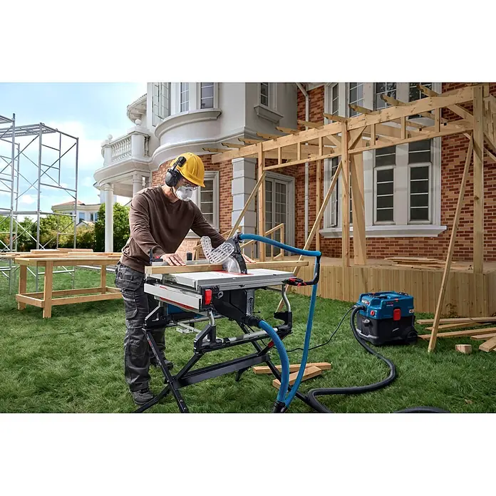 Bosch Professional Tischkreissäge GTS100-254 - 2.200 W, Durchmesser Sägeblatt: 254 mm, Schnitttiefe bei 90 °: 100 mm - Person schneidet Holz mit einer grau-weißen Tischkreissäge. Blauer Absaugschlauch für sauberes Arbeiten angebracht.