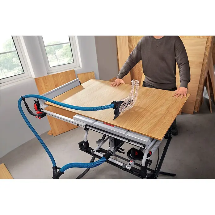 Bosch Professional Tischkreissäge GTS100-254 - 2.200 W, Durchmesser Sägeblatt: 254 mm, Schnitttiefe bei 90 °: 100 mm - Person nutzt eine Tischkreissäge zum Schneiden einer großen Holzplatte. Mit transparentem Sägeblattschutz und blauem Absaugschlauch.