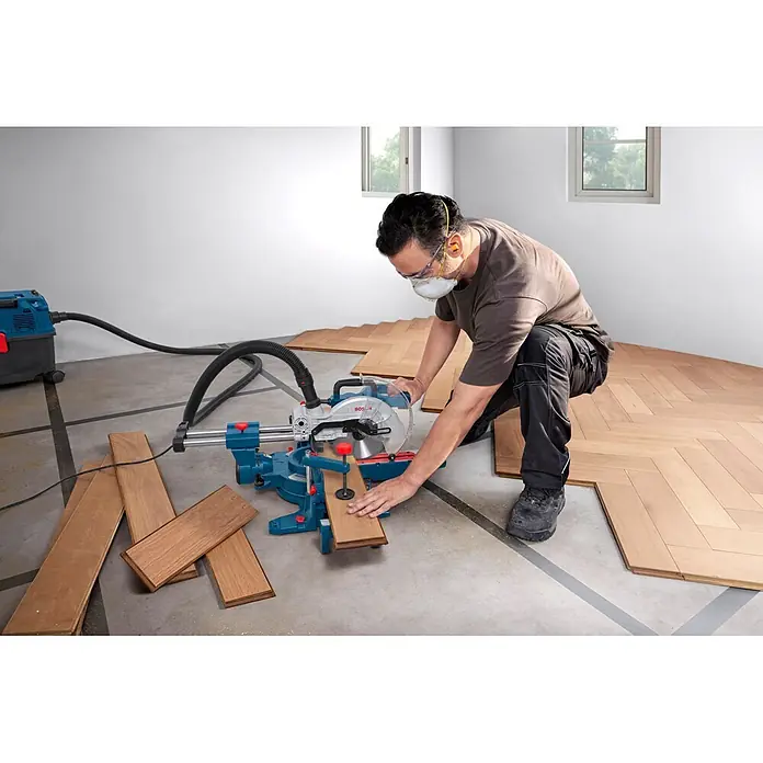 Bosch Professional Kapp- & Gehrungssäge GCM305-216S - 1.300 W, Durchmesser Sägeblatt: 216 mm, Leerlaufdrehzahl: 4.320 U/min - 5.280 U/min - Mann schneidet hellbraune Holzbretter für den Bodenbelag mit einer blauen Bosch Kappsäge.