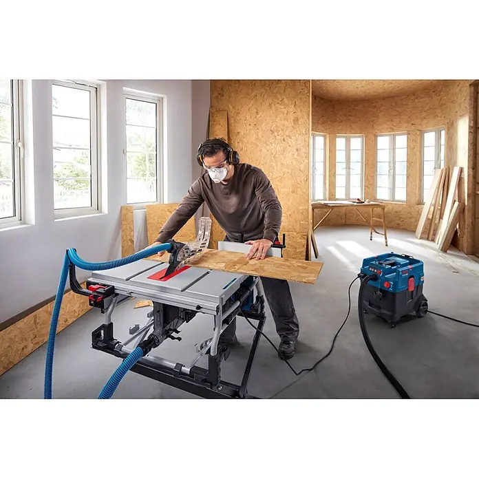Bosch Professional Tischkreissäge GTS100-254 - 2.200 W, Durchmesser Sägeblatt: 254 mm, Schnitttiefe bei 90 °: 100 mm - Mann schneidet Holzbrett an einer Tischsäge, die an einen blauen Staubabsauger angeschlossen ist.