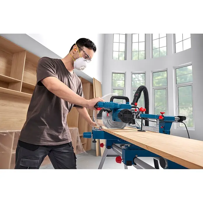 Bosch Professional Kapp- & Gehrungssäge GCM305-216S - 1.300 W, Durchmesser Sägeblatt: 216 mm, Leerlaufdrehzahl: 4.320 U/min - 5.280 U/min - Person schneidet mit blauer und schwarzer Bosch Gehrungssäge ein Holzbrett, trägt Schutzausrüstung.