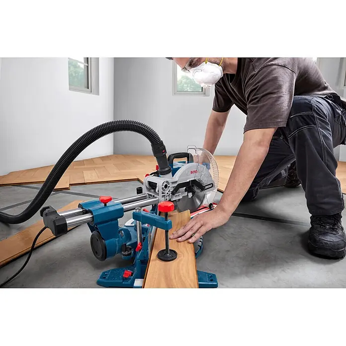 Bosch Professional Kapp- & Gehrungssäge GCM305-216S - 1.300 W, Durchmesser Sägeblatt: 216 mm, Leerlaufdrehzahl: 4.320 U/min - 5.280 U/min - Mann schneidet ein Holzbrett mit einer blau-silbernen Bosch Kappsäge für die Bodenverlegung.