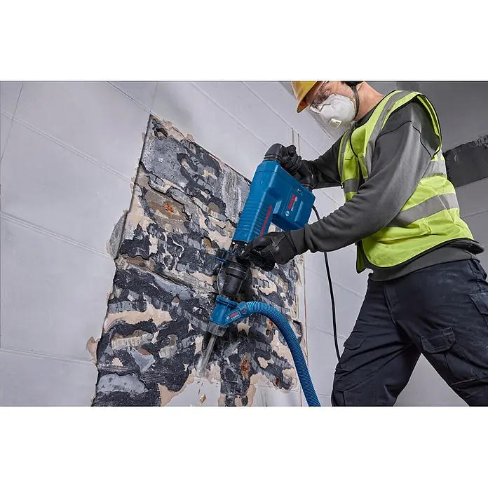Bosch Professional Schlaghammer GSH 11 EV - 16,8 J, Max. Schlagzahl: 1.890 U/min, SDS-Max-Aufnahme - Blauer Bosch Abbruchhammer mit Staubabsaugung, von einem Arbeiter zum Durchbrechen einer Wand verwendet.