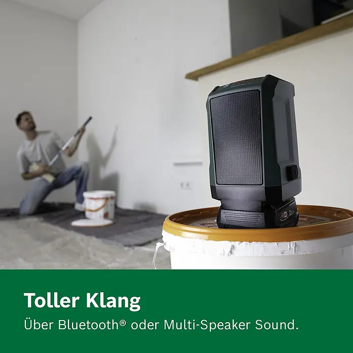 Bosch Power for All 18V Bluetooth-Lautsprecher Universal 18V-1 - 18 V, Ohne Akku - Dunkelgrüner tragbarer Lautsprecher mit schwarzem Gitter und Akku auf einem Farbeimer, während ein Mann streicht.