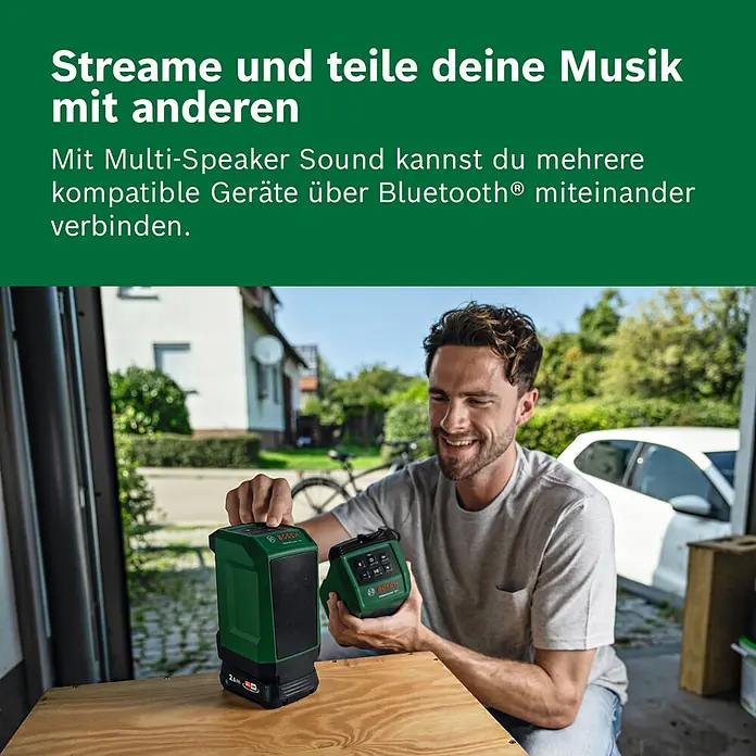 Bosch Power for All 18V Bluetooth-Lautsprecher Universal 18V-1 - 18 V, Ohne Akku - Mann hält zwei grüne Bosch Bluetooth-Lautsprecher, einen mit Akku, auf einem Holztisch zum Musik-Streaming.
