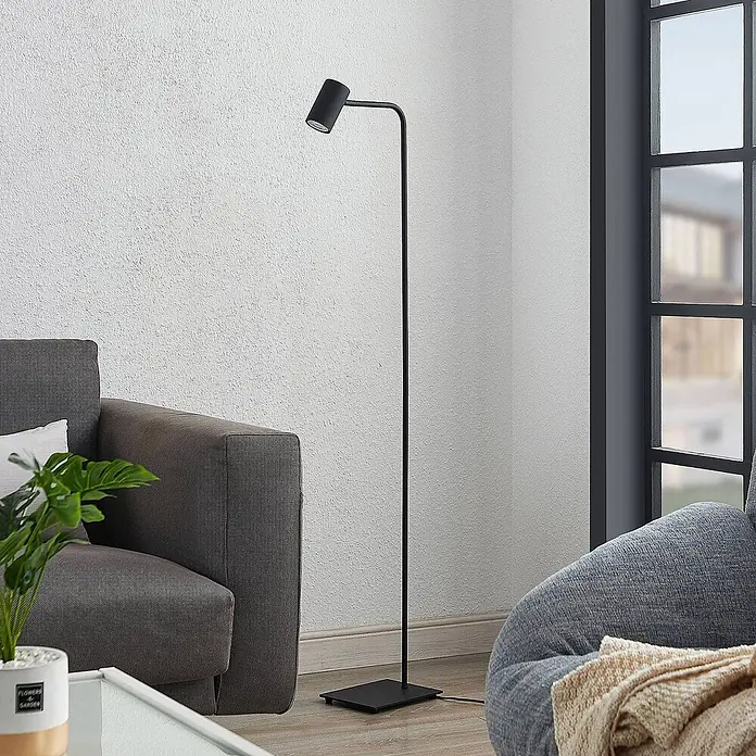 Lindby Stehleuchte Sanad - schwarz, schwarz, GU10 - Eine schlanke, schwarze Metall-Stehlampe mit Spotkopf steht in einem modernen Wohnzimmer.