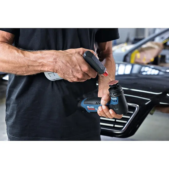 Bosch Professional Akku-Schwingschleifer GSS 12V-32 - 12 V, Anzahl Akkus: Ohne Akku, 6.000 U/min - 16.000 U/min - Eine Person besprüht ein rotes Schleifpad an einem blau-schwarzen Bosch Professional Akku-Exzenterschleifer mit Flüssigkeit.