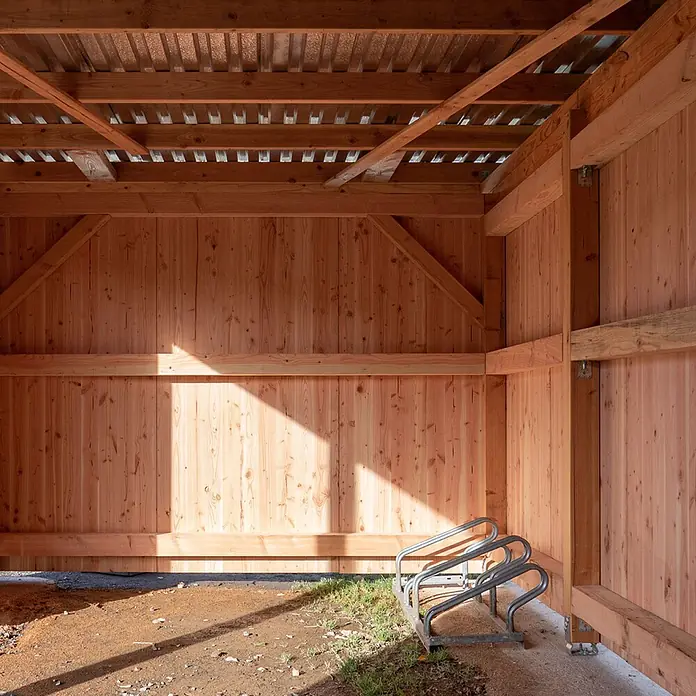 elka 3-Schichtplatte Vita - Douglasie, 2.500 x 660 x 19 mm - Silberner Metall-Fahrradständer für drei Fahrräder in einem Holzunterstand, von Sonnenlicht beschienen.