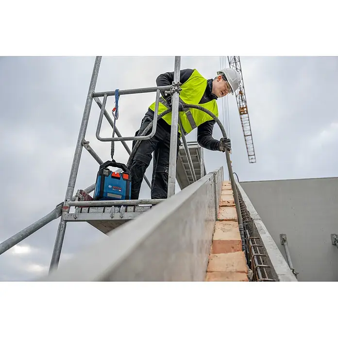Bosch Professional AMPShare 18V Akku-Antriebseinheit Akku-Betonrüttler-System GPU 18V2DI - 18 V, Anzahl Akkus: Ohne Akku, Anzahl benötigte Akkus: 2 Stk. - Blauer und schwarzer Bosch Radio/Ladegerät auf einem Gerüst auf einer Baustelle, neben einem Arbeiter.