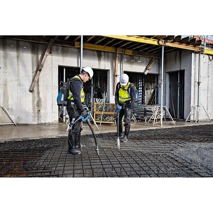 Bosch Professional Innenrüttler Akku-Betonrüttler-System GDI59-65D - Kabellänge: 1 m - Zwei Bauarbeiter verwenden blau-schwarze Betonrüttler mit Rucksack-Stromversorgung auf einer bewehrten Betonplatte.