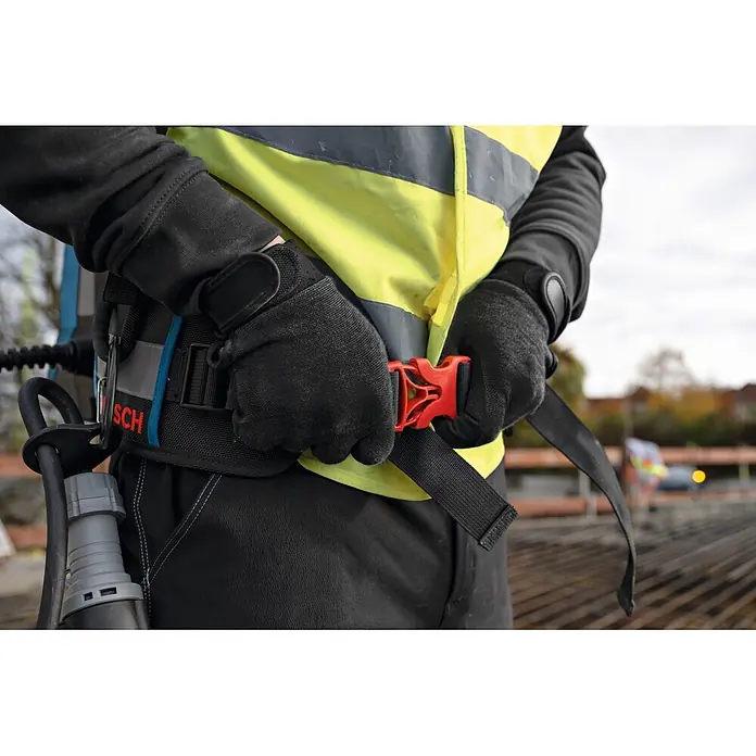 Bosch Professional Tragesystem Akku-Betonrüttler-System GBP100 - 335 x 139 x 540 mm - Person in Arbeitskleidung und Handschuhen befestigt rote Schnellverschluss-Schnalle an schwarzem Arbeitsgürtel mit BOSCH-Komponente.