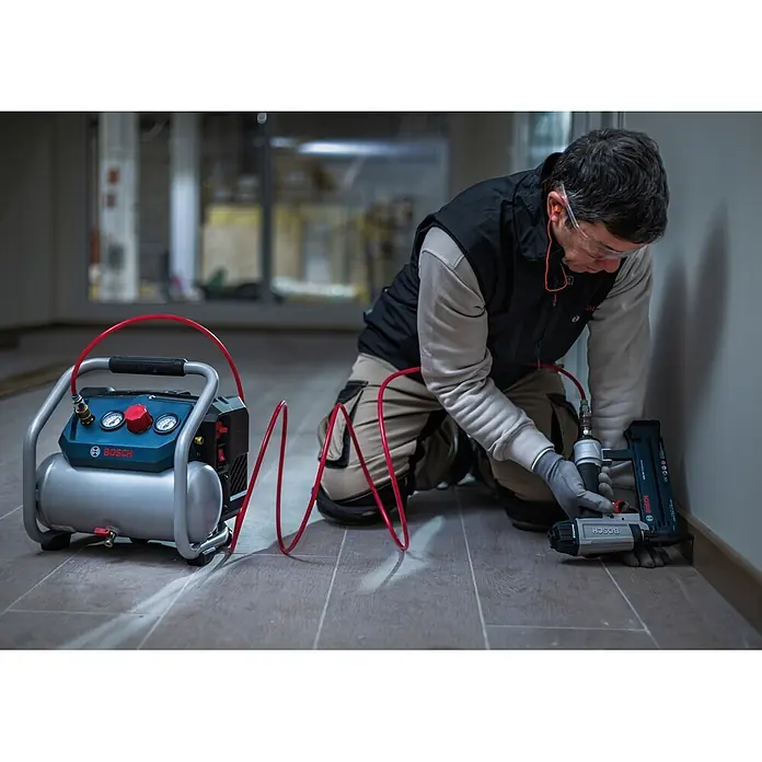 Bosch Professional AMPShare 18V Akku-Kompressor GKO18V-51 - 18 V, 8 bar - Mann nutzt einen blau-silbernen Bosch Luftkompressor mit Bosch Nagelpistole für eine Innenarbeit.