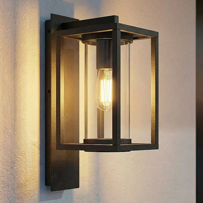 Lucande Außenwandleuchte Ferda - schwarz, schwarz, IP44 - Schwarze Außenwandleuchte aus Metall mit Klarglaszylinder und warmer Edison-LED-Birne an strukturierter Wand.