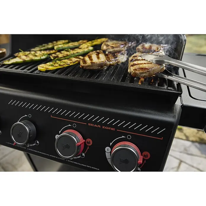 Weber Barbacoa de gas Spirit EPX-435R + Rustidor - Superficie de la parrilla (An x Pr): 61 x 45 cm, 10,3 kW, Número de quemadores: 4 - Primer plano de una parrilla de gas negra con bistecs y calabacines a la parrilla. Unas pinzas voltean un bistec en la 'Sear Zone'.