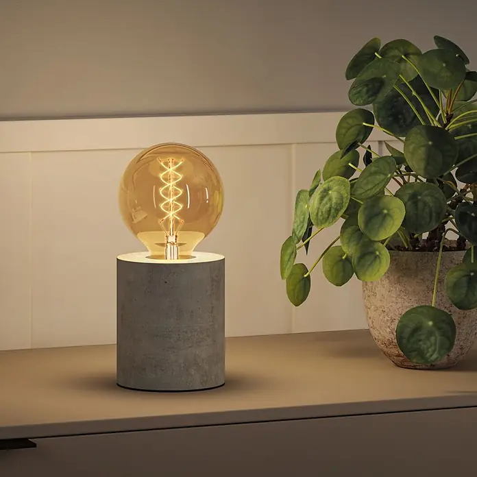 Paulmann LED-Lampe S-Form G95 - E27, Dimmbar, Warmweiß, 300 lm, 4,2 W - Tischleuchte aus Beton mit großer, glühender Amber-Glühbirne auf einer Fläche neben einer Topfpflanze.
