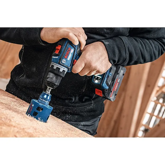 Bosch Professional AMPShare 18V Akku & Ladegerät 1X EXBA 18V-40, GAL 12V/18V - 18 V, 1 Akku, 4 Ah - Eine Person bohrt mit einem blau-schwarzen Bosch Akku-Bohrschrauber und einer blauen Lochsäge in eine Holzoberfläche.