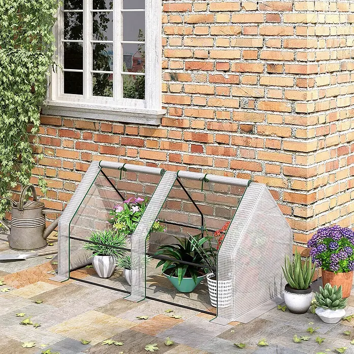 Outsunny Gewächshaus - 180 x 90 cm, Material Seitenwand: Kunststoff, 0,3 mm, Weiß - Zweiteiliges Mini-Gewächshaus mit durchsichtiger Gitterabdeckung und schwarzem Rahmen, beherbergt Topfpflanzen auf einer Terrasse an einer Ziegelwand.