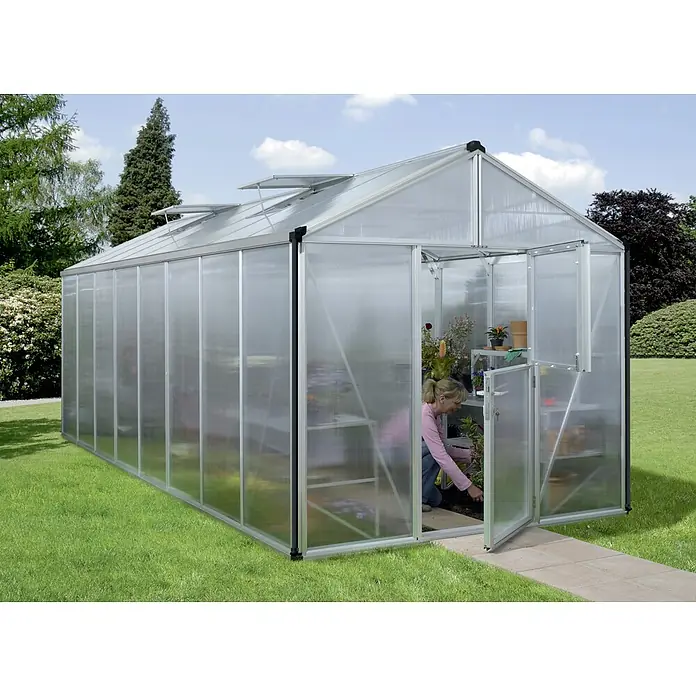 Vitavia Gewächshaus Zeus 15700 Plus - Außenmaß inkl. Dachüberstand (B x T): 256 x 614 cm, 16 mm, Aluminium - Ein großes Gewächshaus mit einer Frau darin, die sich um ihre Pflanzen kümmert. Es bietet ideale Bedingungen für Wachstum.