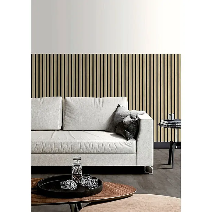 Akustikpaneel Acous Economico - Eiche Hellbraun /schwarzer Filz, 1.200 x 380 x 16,5 mm - Beige Lamellenwandpaneele bilden eine moderne Akzentwand im Wohnzimmer hinter einem weißen Sofa.