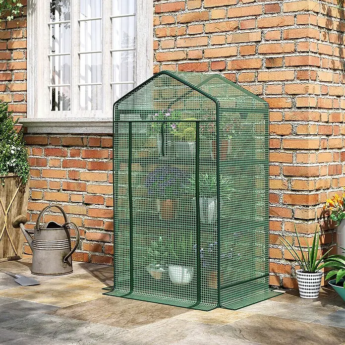 Furnicato Gewächshaus PE-Kunststoff - 49 x 69 cm, Material Seitenwand: Metall, 14 mm, Grün - Kompaktes grünes Maschen-Gewächshaus auf einer Terrasse, gefüllt mit Topfpflanzen, neben einem Ziegelhaus.