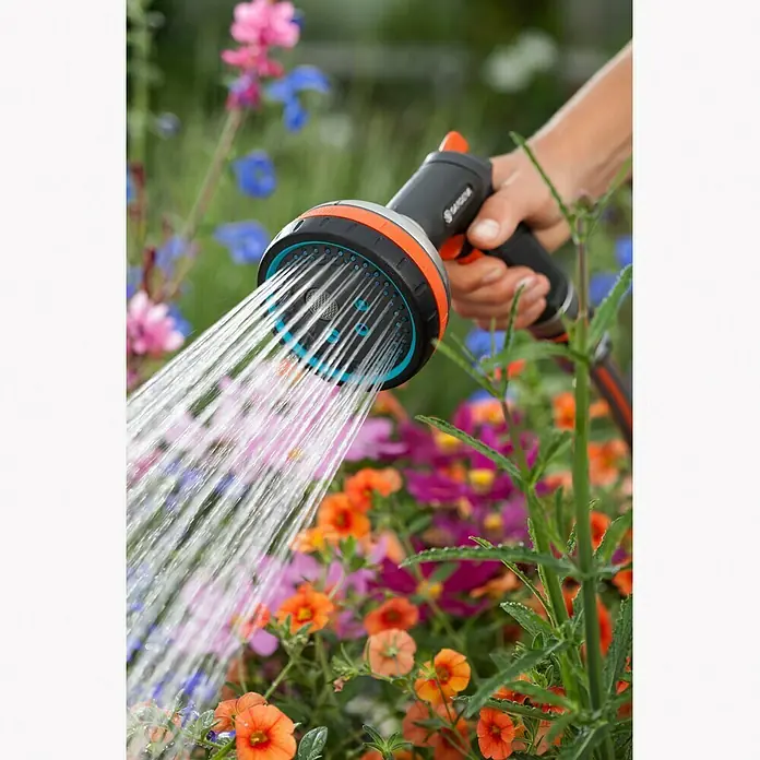 Gardena Premium Multibrause - Anzahl Sprühformen: 5 Stk., Metall/Kunststoff - Die Hand hält eine Gardena-Gartendusche, die Wasser auf ein Blumenbeet sprüht. Ideal für die Gartenbewässerung mit verschiedenen Strahlarten.