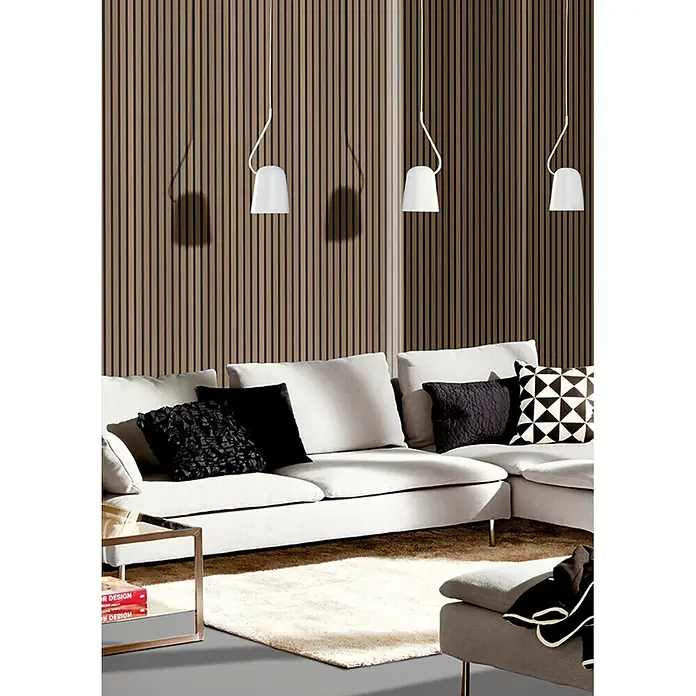 acous Akustikpaneel Economico - Eiche rustikal / schwarzer Filz, 2.400 x 380 x 16,5 mm - Modernes Wohnzimmer mit heller Eckcouch, Zierkissen, beleuchtet von drei weißen Pendelleuchten vor einer Lattenholzwand.