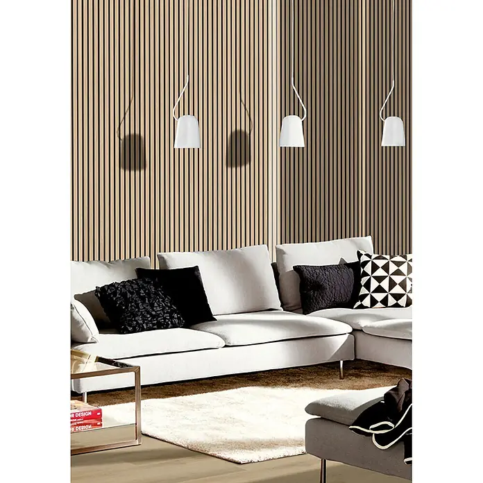 acous Akustikpaneel Economico - Eiche Hellbraun /schwarzer Filz, 2.400 x 380 x 16,5 mm - Modernes Wohnzimmer mit hellgrauem Ecksofa, schwarzen Kissen und weißen Pendelleuchten vor einer Holzlamellenwand.