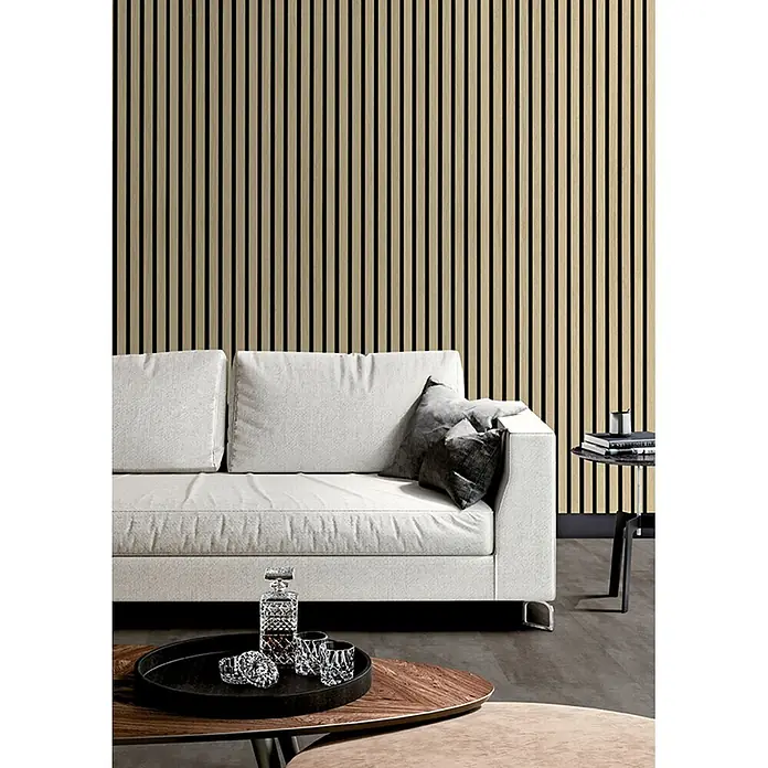 acous Akustikpaneel Economico - Eiche Hellbraun /schwarzer Filz, 2.400 x 380 x 16,5 mm - Akustische Lamellenwandverkleidung aus hellem Holz hinter einem weißen Sofa in einem modernen Wohnzimmer.