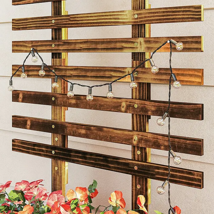 Outsunny Hochbeet - 65 x 31 x 147 cm, Holz, Braun - Lichterkette mit klaren Glühbirnen an dunklem Kabel, über Holzspalier drapiert, mit Blumen darunter.