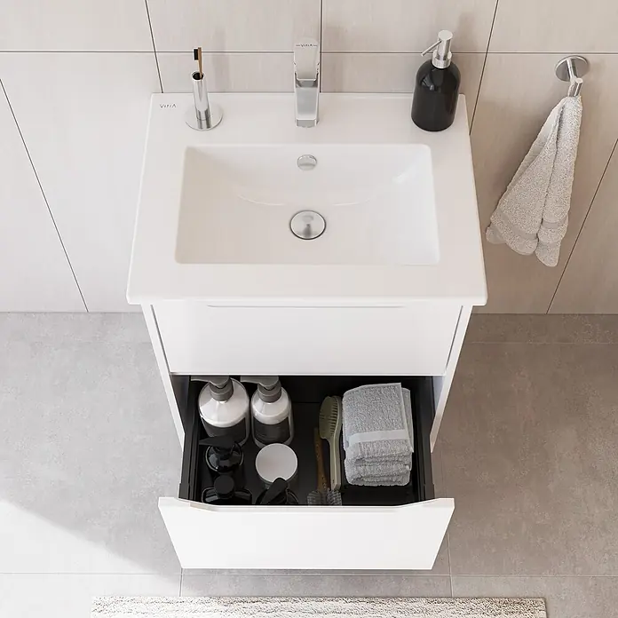 VitrA Integra Square Badmöbel-Set - Gesamtbreite Badmöbel: 60 cm, Weiß, Matt - Weißer Badschrank mit integriertem Waschbecken und offener Schublade, die Pflegeprodukte und Handtücher in einem modernen Badezimmer zeigt.