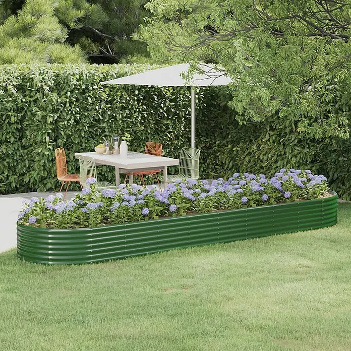 Furnicato Hochbeet - 396 x 396 x 36 cm, Stahl, Grün - Grünes Hochbeet aus gewelltem Metall, gefüllt mit lila Blumen, auf einem Rasen neben einem Terrassen-Essbereich.