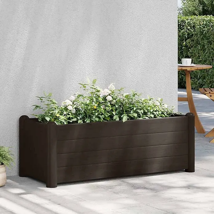 Furnicato Hochbeet - 100 x 43 x 35 cm, Kunststoff, Mokka - Dunkelbrauner Blumenkasten aus Holz mit grünen Pflanzen und weißen Blüten auf einer Terrasse.