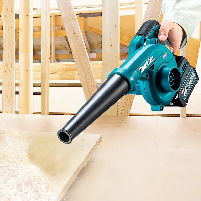 Makita XGT 40V max. Akku-Gebläse UB002GZ01 - 40 V, Ohne Akku, Blasgeschwindigkeit: 99 m/s - Türkiser und schwarzer Makita Akku-Gebläse in der Hand, bläst Sägemehl von einem Holzbrett.