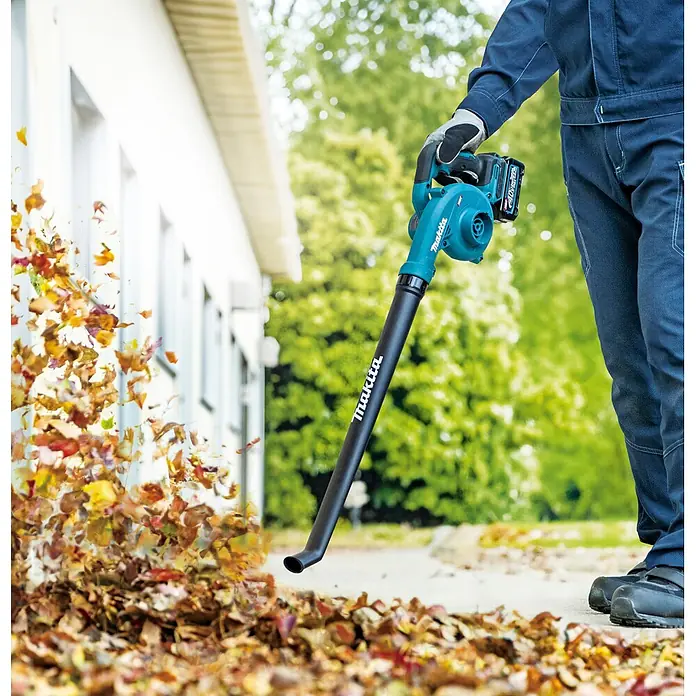 Makita XGT 40V max. Akku-Gebläse UB002GZ01 - 40 V, Ohne Akku, Blasgeschwindigkeit: 99 m/s - Eine Person in Arbeitskleidung bläst mit einem blau-schwarzen Makita Laubbläser Herbstlaub von einem Weg.