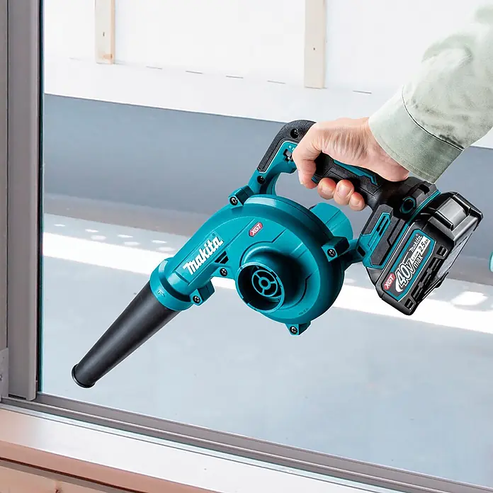 Makita XGT 40V max. Akku-Gebläse UB002GZ01 - 40 V, Ohne Akku, Blasgeschwindigkeit: 99 m/s - Eine Hand hält einen türkisfarbenen und schwarzen Makita Akku-Bläser mit XGT 40V Batterie, auf ein Fenster gerichtet, bereit zum Einsatz.