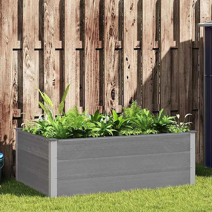 Furnicato Hochbeet - 150 x 100 x 54 cm, Verbundwerkstoff, Grau - Graues Hochbeet aus Verbundwerkstoff gefüllt mit Grünpflanzen, im Garten vor einem Holzzaun stehend.