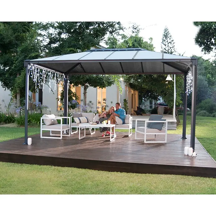 Palram – Canopia Pérgola estándar Martinique - An x Pr: 430 x 295 cm, Color del armazón: Antracita, Aluminio - Cenador gris oscuro con techo gris claro que protege a una pareja relajándose en una terraza de madera exterior.