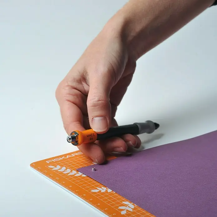 Fiskars Ösenstanzer - 2 -tlg. - Nahaufnahme eines Fiskars-Werkzeugs mit Rollklinge zum präzisen Schneiden von Papier auf einer Schneidematte.