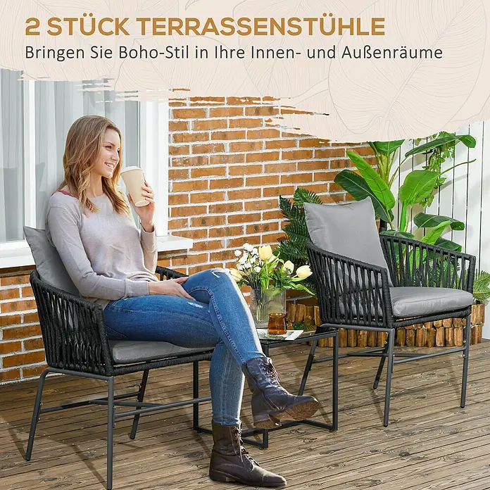 Outsunny Gartenstuhl-Set 2-Stück im Boho-Design - 2 Stk., Stahl, Polyester, Polyethylen, Schwarz, Grau - Zwei dunkle, geflochtene Terrassenstühle mit grauen Kissen und einem kleinen Tisch auf Holzterrasse, ein Stuhl von Frau besetzt.