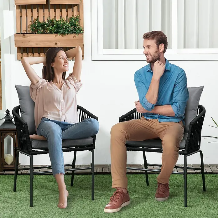 Outsunny Gartenstuhl-Set 2-Stück im Boho-Design - 2 Stk., Stahl, Polyester, Polyethylen, Schwarz, Grau - Zwei Personen entspannen auf schwarzen Outdoor-Stühlen mit geflochtenen Rückenlehnen und grauen Kissen.
